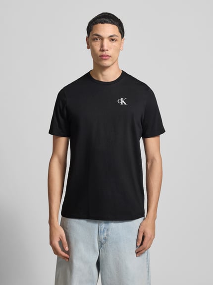 Männermodel trägt Regular Fit T-Shirt mit Logo-Print von Calvin Klein Jeans in Schwarz, reine Baumwolle, Rundhalsausschnitt, Ganzkörperansicht von vorne.