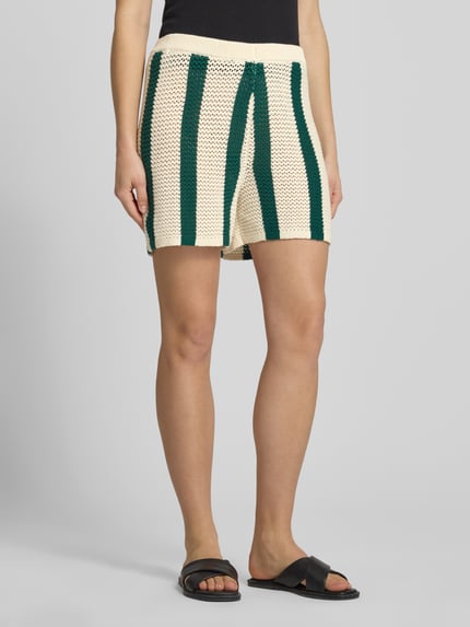 Frauenmodel trägt Regular Fit Sweatshorts aus reiner Baumwolle Modell 'KENZIE' von Pieces, Optik: Allover-Muster, Muster: gestreift, Materialverarbeitung: Strick, Farbe creme mit grünen Streifen, Bundabschluss: elastisch, Nahaufnahme Unterkörper.