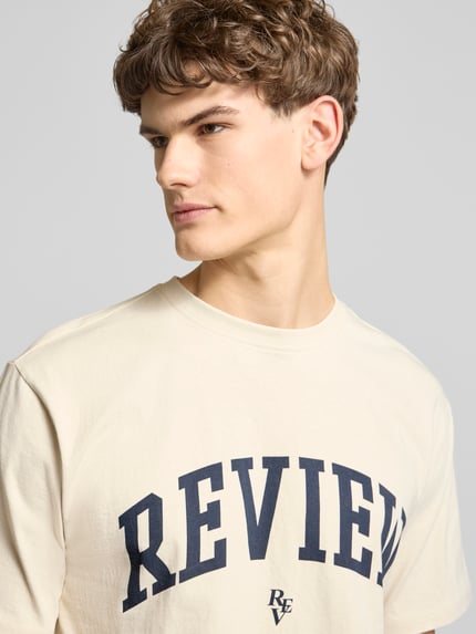 Mannenmodel draagt T-Shirt met Label-Print en Rundhalsausschnitt van REVIEW, katoen, regular fit, label-print, crèmekleurige stof, close-up bovenlichaam.