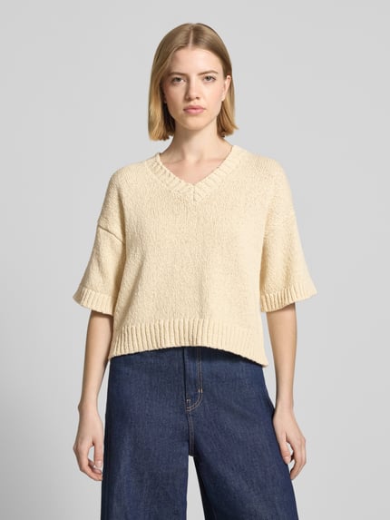 Frauenmodel trägt Regular Fit Pullover in Strick-Optik Modell 'Hannalie' von MSCH Copenhagen aus Reine Baumwolle, Halbarm, V-Ausschnitt, beige Farbe, strukturierte Oberfläche, Ganzkörperansicht von vorne.