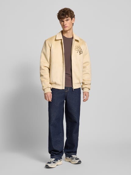 Männermodel trägt Jacke in Leder-Optik mit Label-Stitching von KARL KANI, Material-Mix mit Stretch-Anteil, Regular Fit, Beige, Ganzkörperansicht von vorne.