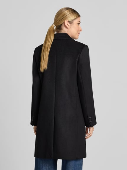 Frauenmodel trägt Regular Fit Mantel mit Reverskragen Modell 'DALI' von MANGO in Schwarz, glatte Textur, Rückenansicht, Kontext: Damen Mantel, 2-Knopfleiste, Rückenlänge 93 cm, Schulterbreite 38 cm, Brustweite 47 cm, Ärmellänge 60 cm.