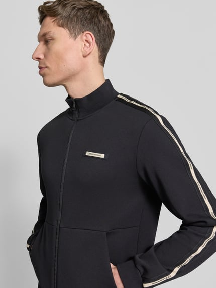 Männermodel trägt schwarze Sweatjacke mit Stehkragen und Zweiwege-Reißverschluss von EA7 Emporio Armani, Nahaufnahme Oberkörper.