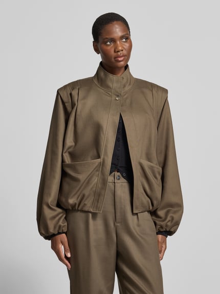 Frauenmodel trägt Funktionsjacke mit großen Fronttaschen von black palms in unifarbener Optik, Struktur, Loose Fit, Stehkragen, Ganzkörperansicht von vorne.