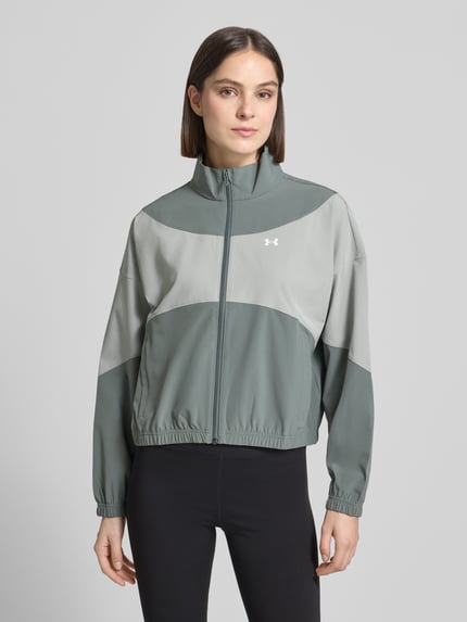 Kobiece model prezentuje kurtka treningowa z stójką i wpuszczanymi kieszeniami od Under Armour, krój regular fit, logo, zamek błyskawiczny, długość tyłu w rozmiarze S: 60 cm, szerokość ramion w rozmiarze S: 62 cm, szerokość klatki piersiowej w rozmiarze S: 57 cm, długość rękawów w rozmiarze S: 50 cm, odcienie szarości, tekstura gładka, całkowity widok z przodu
