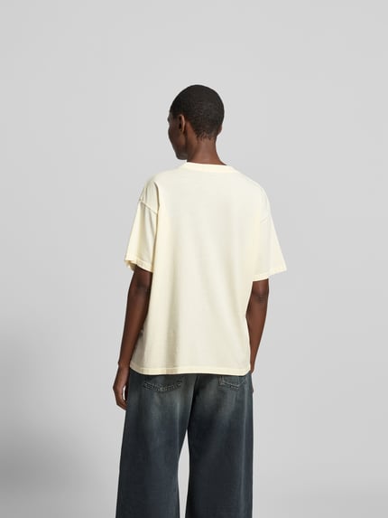 Frauenmodel trägt Regular Fit T-Shirt mit Logo-Print von Anine Bing aus reiner Baumwolle, sanftes Gelb, Rückenansicht, Rückenlänge 60 cm. Ganzkörperansicht Rückansicht.