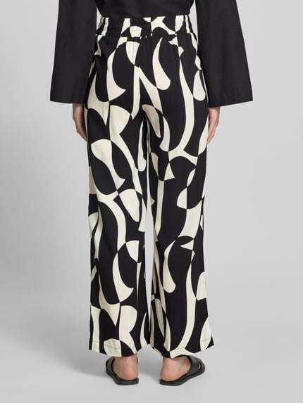 Frauenmodel trägt Stoffhose aus Viskose im Allover-Look Modell 'CHANISE' von Soyaconcept, Schwarz-Weiß, Relaxed-Fit, Ganzkörperansicht Rückansicht. Bundweite bei Größe S: 35 cm, Innenbeinlänge: 76 cm.