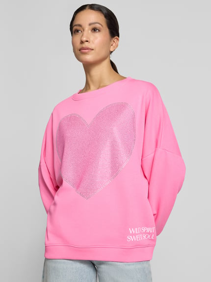 Vrouwenmodel draagt oversized sweatshirt uit puur katoen Model 'Sweet Soul' van miss goodlife in felroze met strass-steentjes en statementprint. Nahaufnahme Oberkörper.