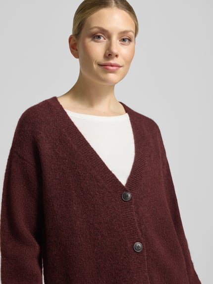 Frauenmodel trägt Cardigan aus Wolle mit Logo-Stitching Modell 'Sirala' von HUGO in Bordeaux, Strickoptik, Nahaufnahme Oberkörper.