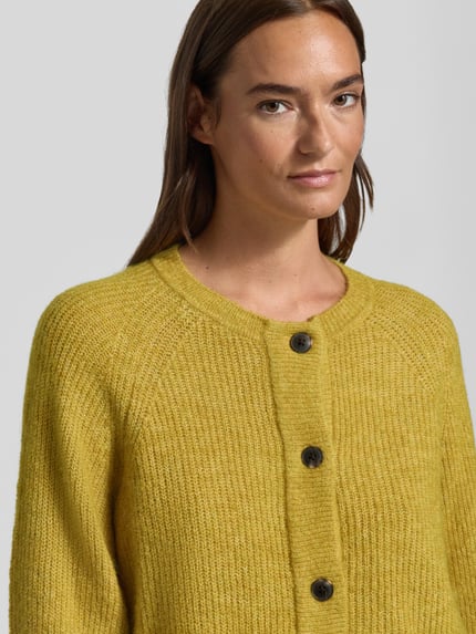Frauenmodel trägt Relaxed Fit Strickjacke aus Woll-Mix Modell 'LULU' von Selected in Senfgelb mit grober Strickstruktur, Nahaufnahme Oberkörper, Damen Strickjacke von Selected.