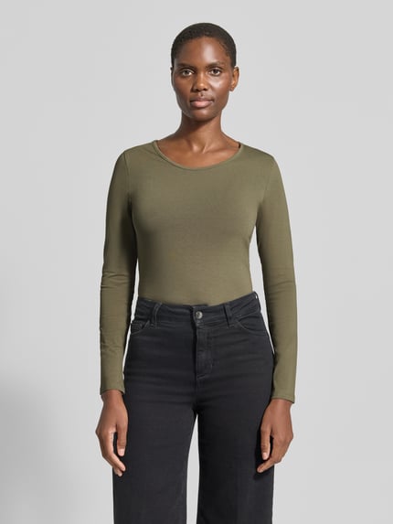 Frauenmodel trägt Longsleeve mit Rundhalsausschnitt von ZABAIONE in Oliv, taillierter Schnitt, glatte Textur, Ganzkörperansicht von vorne. Baumwoll-Elasthan-Mix, Rückenlänge bei Größe S: 55 cm.
