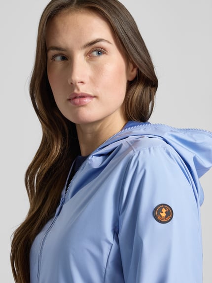 Vrouwenmodel draagt Regular Fit Jacke met Tweewegritssluiting Modell 'Stella' van SAVE THE DUCK in lichtblauw, detailopname schouder en borst, context: dames jack met ritssluitingen, ruglengte 60 cm, schouderbreedte 42 cm, borstwijdte 52 cm, mouwlengte 64 cm.