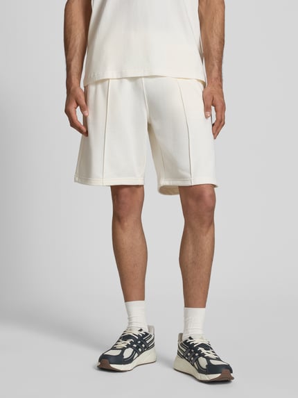 Männermodel trägt Bermudas mit elastischem Bund und Label-Stitching von CHAMPION, Baumwoll-Mix, Regular Fit, Längsnähte, Ganzkörperansicht von vorne.