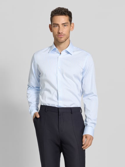 Männermodel trägt Regular Fit Businesshemd mit extra langem Arm Modell 'H-JOE-K' von BOSS, gestreift, Kentkragen, Ganzkörperansicht von vorne.