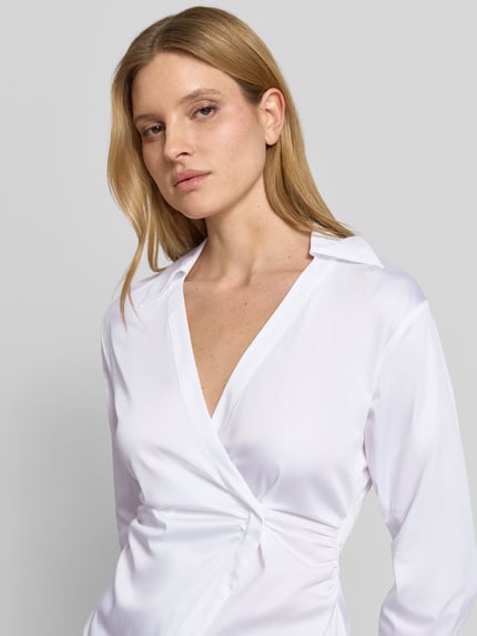 Vrouwenmodel draagt Bluse mit Raffungen und V-Ausschnitt van comma, wit met taille fit, katoenmix met stretch, reverskraag, detailopname bovenlichaam.