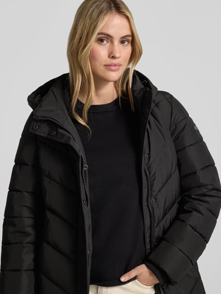 Frauenmodel trägt Jacke mit abnehmbarer Kapuze von NAUTGÅRD in Schwarz mit gestrickten Ärmelabschlüssen, Nahaufnahme Oberkörper.