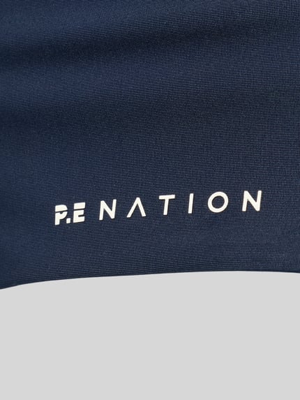 Produktfoto, Detailansicht des Logos auf dunkelblauem, strukturiertem Stoff des Sport-BH mit Racerback Modell 'ACTIVE' von P.E Nation, Material-Mix mit Stretch-Anteil und Logo-Print.