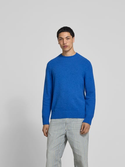 Męski model nosi Relaxed Fit Pullover in Strick-Optik od Forét w intensywnie niebieskim kolorze, bawełniana mieszanka, bouclé, okrągły dekolt, widoczna struktura materiału, długość tyłu w rozmiarze M: 66 cm, krój relaxed fit, widok całej sylwetki z przodu.