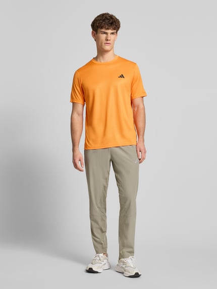 Männermodel trägt T-Shirt mit Logo und Rundhalsausschnitt von adidas Training in Orange, Regular Fit, Ganzkörperansicht von vorne.