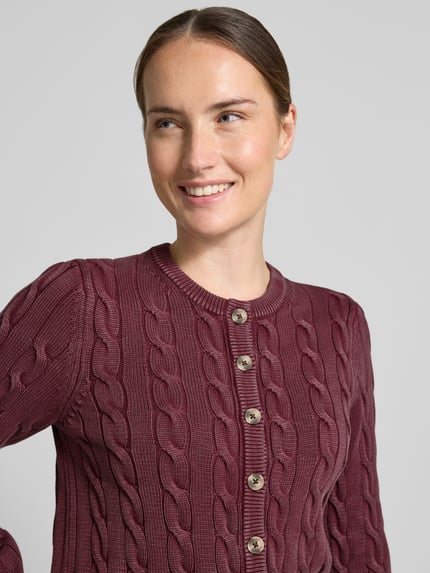 Frauenmodel trägt Relaxed Fit Strickjacke aus reiner Baumwolle von Jake*s Casual in Dunkelrot mit Zopfmuster und Knöpfen, Nahaufnahme Oberkörper.