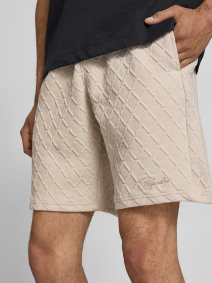 Männermodel trägt Relaxed Fit Shorts mit Strukturmuster Modell 'Jovren' von Pegador, Beige, Elastischer-Material-Mix, Nahaufnahme Oberschenkel, Herren Shorts, Bundweite 39 cm, Innenbeinlänge 24 cm, Größe M.