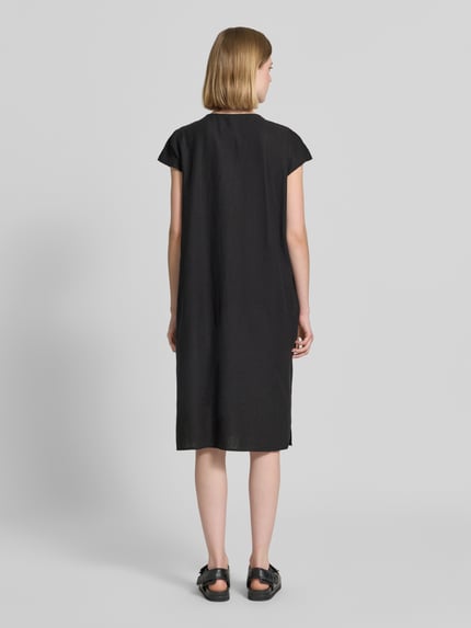 Vrouwenmodel draagt knielang leinenkleed met V-hals model 'Ina' van Soyaconcept, loose fit, zwarte kleur, rugaanzicht, context: dames leinenkleed, linnenmix met viscose, zijsplitten, ruglengte maat S 105 cm, borstwijdte 51 cm, mouwlengte 7 cm.