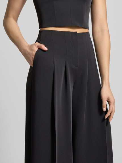 Vrouwenmodel draagt Stoffhose mit weitem Bein und gelegten Falten van Jake*s Cocktail, zwart, stretch, geplooid, detailopname taille en benen.