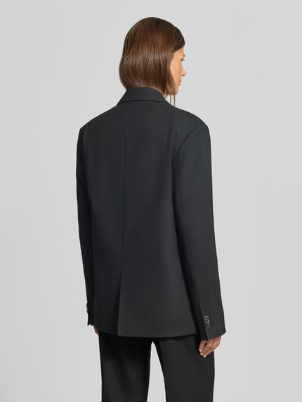 Vrouwenmodel draagt Relaxed Fit Blazer met viscose van MYON, zwarte kleur, reverskraag, dubbele knoopsluiting, elastische materiaalmix, Ruglengte 72 cm, Borstwijdte 48 cm, Mouwlengte 63 cm, relaxed fit, Ganzkörperansicht Rückansicht