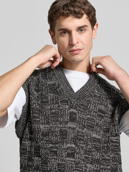Männermodel trägt Regular Fit Pullunder aus Baumwolle von Filippa K in Schwarz-Grau mit Strukturmuster, Nahaufnahme Oberkörper.