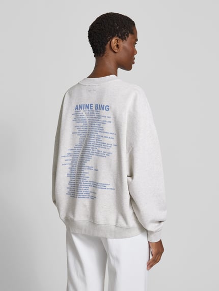 Frauenmodel trägt Relaxed Fit Sweatshirt mit Logo-Print von Anine Bing aus bawełna, krój relaxed fit, nadruk z logo, okrągły dekolt, elastyczne wykończenia, długość tyłu w rozmiarze S 61 cm, jasnoszary materiał, nadruk z napisem na plecach, Ganzkörperansicht Rückansicht.