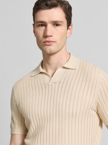 Męski model nosi Slim Fit Poloshirt mit V-Ausschnitt von Profuomo, mieszanka bawełny i lnu, kołnierzyk polo, dekolt w serek, krój slim fit, długość tyłu w rozmiarze M: 67 cm, kremowe pionowe prążki, nadany miękki wygląd, zbliżenie na górną część ciała.