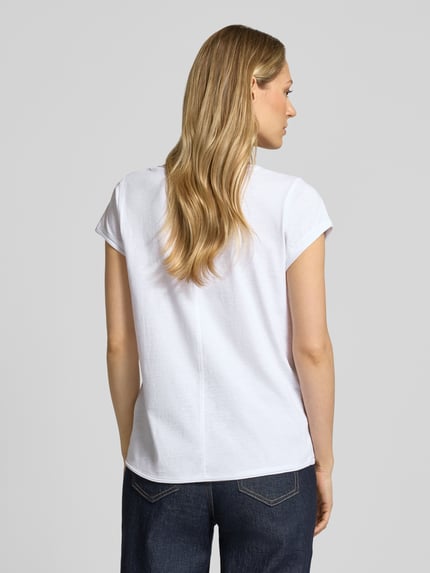 Modelka prezentuje damski t-shirt 'T-Shirt mit V-Ausschnitt' od Christian Berg Woman z bawełny, krój regular fit, dekolt w serek, zrolowany brzeg, długość tyłu w rozmiarze S: 59 cm, widok całej sylwetki z tyłu.