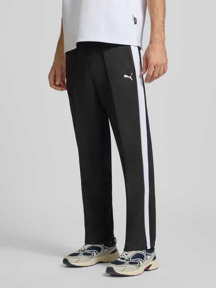 Männermodel trägt Relaxed Fit Jogginghose mit Baumwoll-Anteil Modell 'T7 ALWAYS ON' von PUMA Performance, Schwarz mit weißem Streifen, Ganzkörperansicht von vorne.