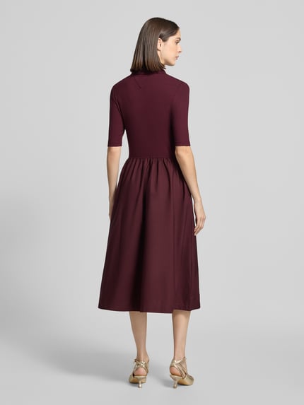 Frauenmodel trägt Midikleid mit Polokragen von Tommy Hilfiger in Dunkelrot, strukturierter Stoff, Ganzkörperansicht Rückansicht.