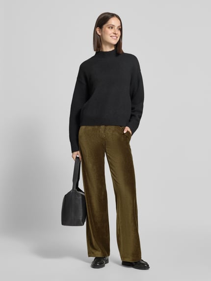 Frauenmodel trägt Regular Fit Cordhose mit Bundfalten Modell 'MAINE' von BRAX in unifarbener Optik, Cordstruktur, seitliche Eingrifftaschen und Gesäßtaschen, Verschluss mit Knopf und verdecktem Reißverschluss, Gürtelschlaufen, Ganzkörperansicht von vorne.