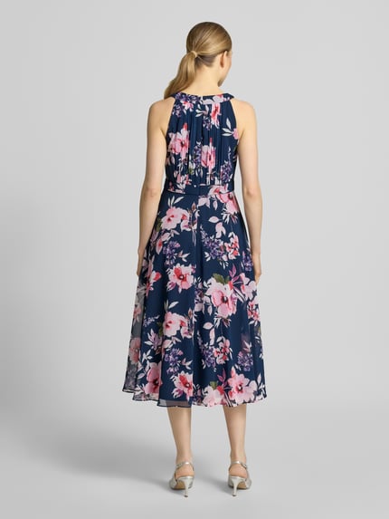 Frauenmodel trägt Midikleid mit floralem Allover-Print von Christian Berg Cocktail in Dunkelblau, Taillierte Passform, Rundhalsausschnitt, Gelegte Falten, Ärmelloses-Design, Nahtreißverschluss, Ganzkörperansicht Rückansicht.