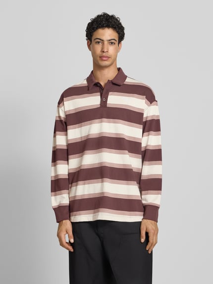 Mężczyzna model nosi Regular Fit Poloshirt mit elastischen Ärmelabschlüssen von PUMA PERFORMANCE z bawełny, krój regular fit, kołnierzyk polo, z długim rękawem, beżowo-brązowe pasy, długość tyłu 75 cm, długość rękawów 59 cm, Ganzkörperansicht von vorne.