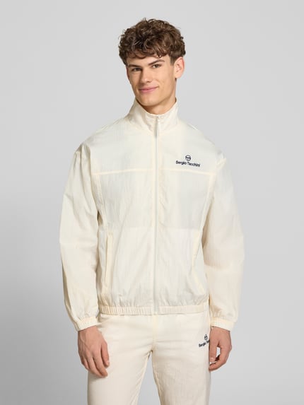 Männermodel trägt Regular Fit Jacke mit Stehkragen Modell 'Nayla' von SERGIO TACCHINI, creme, Reißverschluss, Eingrifftaschen, elastische Abschlüsse, Ganzkörperansicht von vorne, Kontext: Rückenlänge bei Größe M 69 cm, Ärmellänge 61 cm.