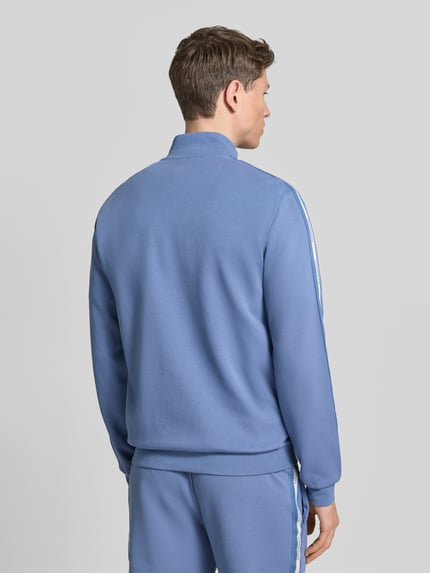 Männermodel trägt Sweatjacke aus Baumwoll-Mix von EA7 Emporio Armani in Blau mit Galonstreifen, elastischen Abschlüssen, Rückenansicht.