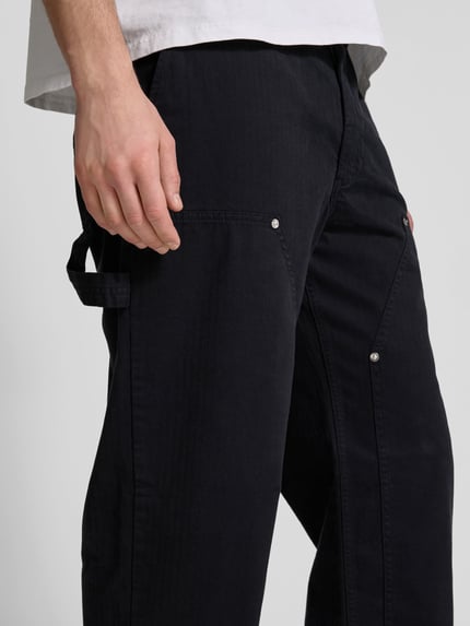 Männermodel trägt Relaxed Fit Hose mit Steekzakken en labeldetail van Wood Wood, mix van katoen en elastaan, donker, detailaufnahme.