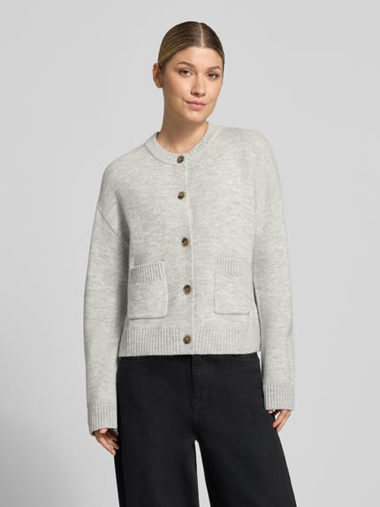 Frauenmodel trägt Cardigan mit aufgesetzten Taschen von Christian Berg Woman in unifarbener Strickoptik, Ganzkörperansicht von vorne.