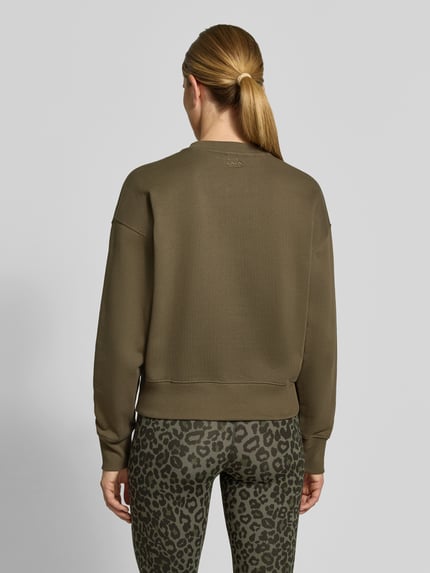 Frauenmodel trägt Sweatshirt mit Label-Print von Lala Berlin aus reiner Baumwolle in Olivgrün, lockerer Schnitt, gerippte Abschlüsse, Ganzkörperansicht Rückansicht.