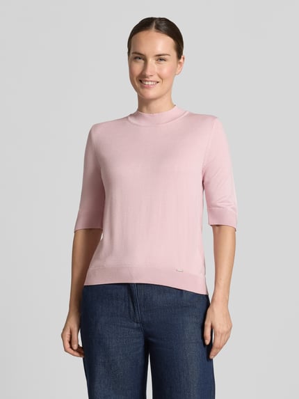 Frauenmodel trägt Strickpullover aus Viskose-Mix von MORE & MORE in Rosa mit Stehkragen, gerippten Abschlüssen und Halbarm, taillierte Passform, Ganzkörperansicht von vorne.