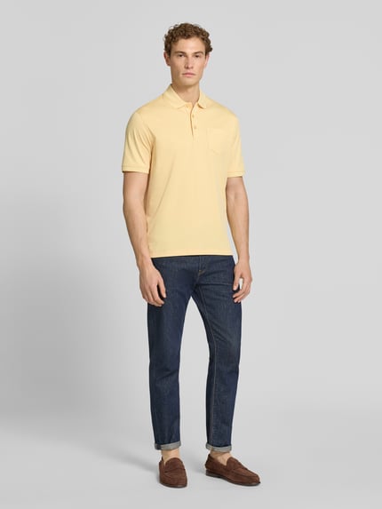 Männermodel trägt Regular Fit Poloshirt mit Brusttasche und Label-Stitching von bugatti in Gelb, kombiniert mit Jeans; Ganzkörperansicht von vorne. Rückenlänge bei Größe M: 70 cm, Knopfleiste, Polokragen.