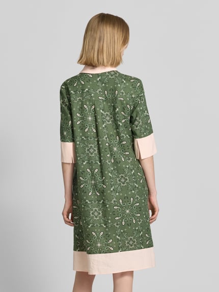 Frauenmodel trägt knielanges Kleid mit Polokragen und kurzer Knopfleiste von Christian Berg Woman Selection im Leinen-Mix, gerader Schnitt, grünes Muster mit beigen Abschlüssen, Ganzkörperansicht Rückansicht.