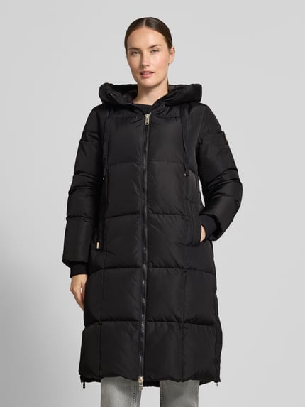 Kobiece model prezentuje Regular Fit płaszcz w stylu z efektem pikowania Model 'Nova' od MOS MOSH, czarny, wpuszczane kieszenie, kaptur z tunelem, zamek błyskawiczny dwustronny, Długość tyłu w rozmiarze S: 102 cm, Szerokość ramion w rozmiarze S: 42 cm, Szerokość w rozmiarze S: 46 cm, Długość rękawów w rozmiarze S: 64 cm, widok całej sylwetki z przodu.