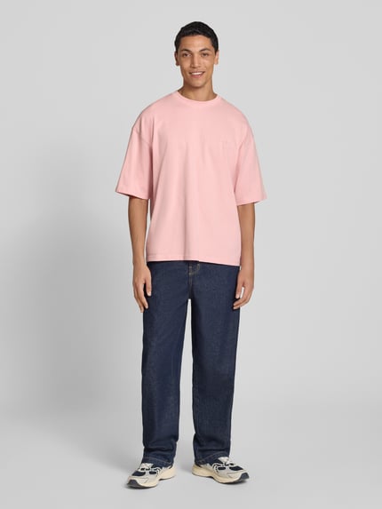 Männermodel trägt Oversized T-Shirt aus reiner Baumwolle von REVIEW in Rosa, Rundhalsausschnitt, lockere Passform, Ganzkörperansicht von vorne.