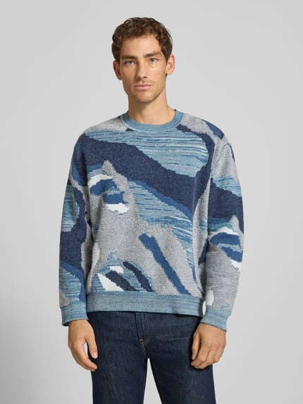 Męski model nosi Loose Fit Strickpullover im Allover-Look von Scotch & Soda, mieszanka bawełny, wzór na całej powierzchni, okrągły dekolt, długość tyłu w rozmiarze M: 65 cm, długość rękawów w rozmiarze M: 60 cm, odcienie niebieskiego i szarości, faktura dzianinowa, Ganzkörperansicht von vorne.