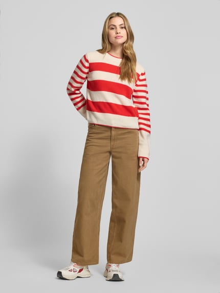 Vrouwenmodel draagt Regular Fit Strickpullover aus reiner Schurwolle van Marc O'Polo met rood-beige gestreept patroon, geribbelde boorden, crew neck en lange mouwen, gebreide structuur, voorkant hele lichaam.