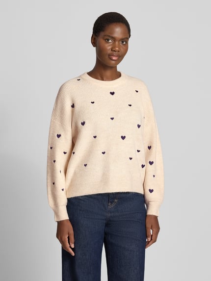Frauenmodel trägt Strickpullover mit Woll-Anteil von Apricot in Beige mit Ripp-Optik, Herz-Stitchings, lockerer Passform, Ganzkörperansicht von vorne.